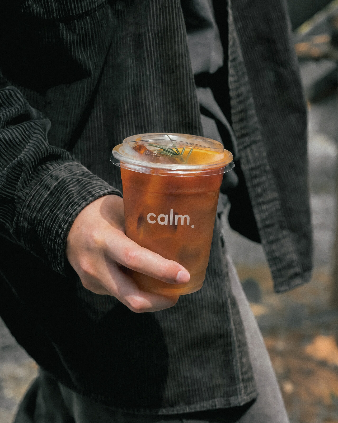 A person holding a Calm.-branded iced drink garnished with rosemary and orange