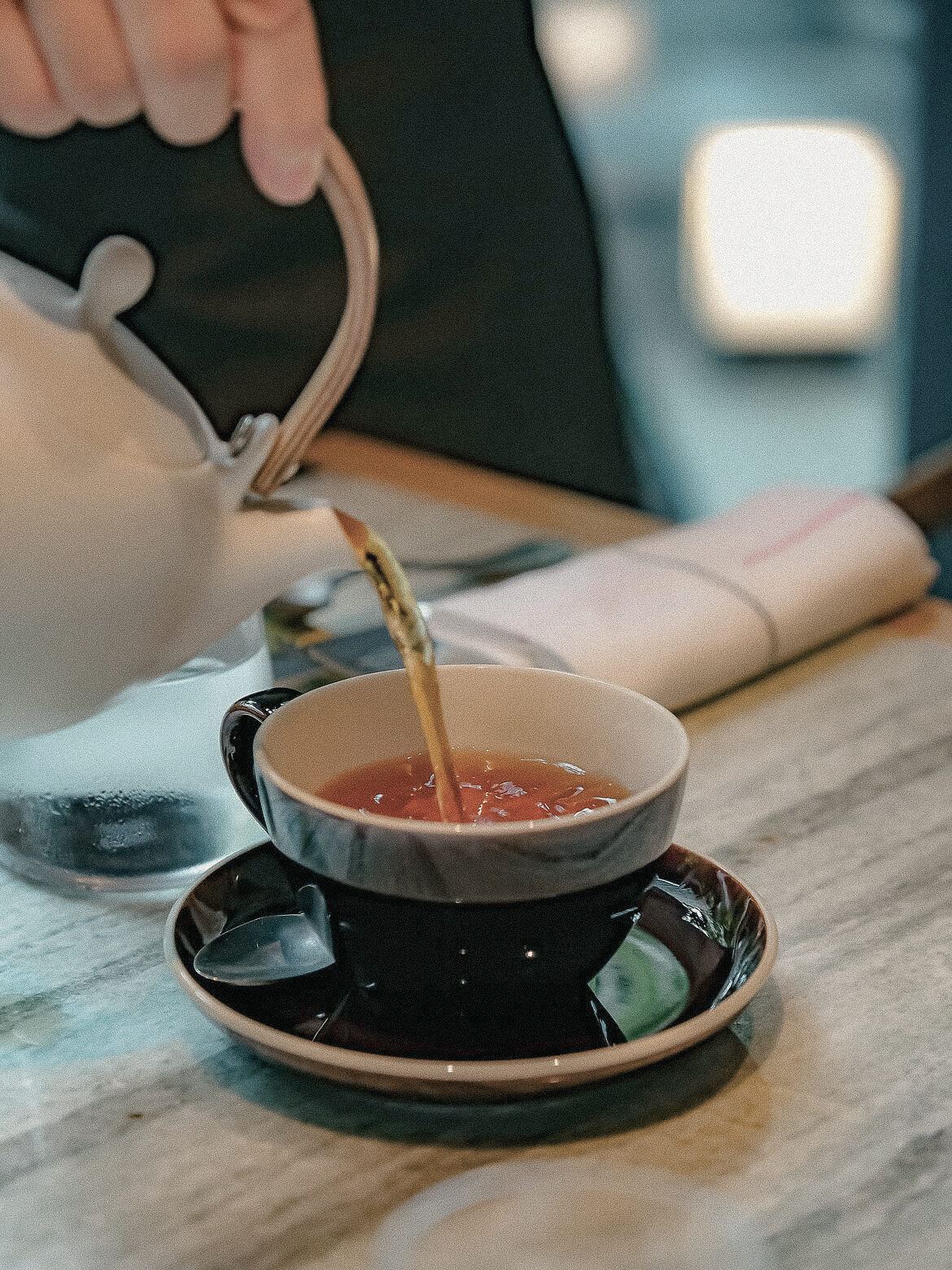 Amber tea being poured from a white teapot into a dark cup